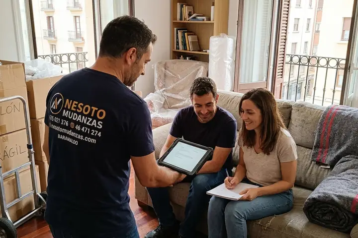 Operario de NESOTO enseñando con una tablet el presupuesto de una mudanza a una pareja en su salón con cajas