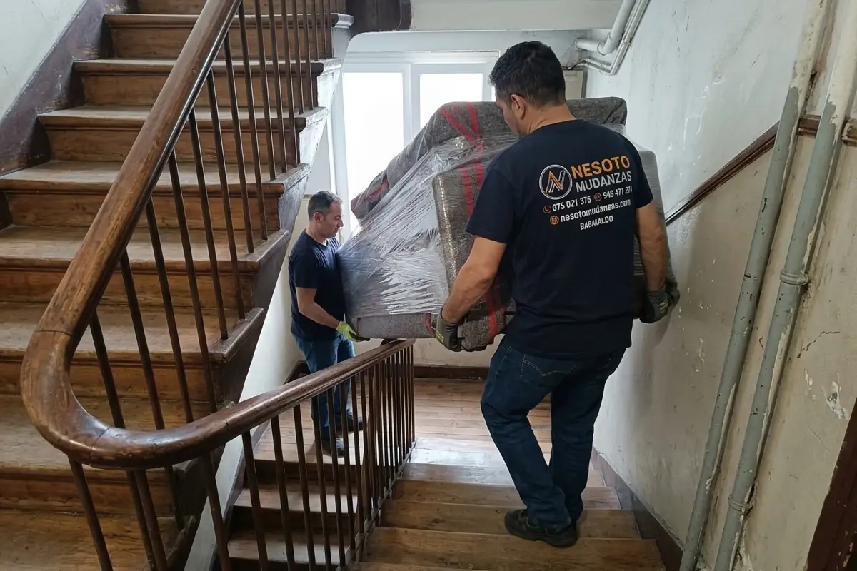 Mudanza de piso en Bilbao: dos operarios de NESOTO bajando un sofá protegido por la escalera