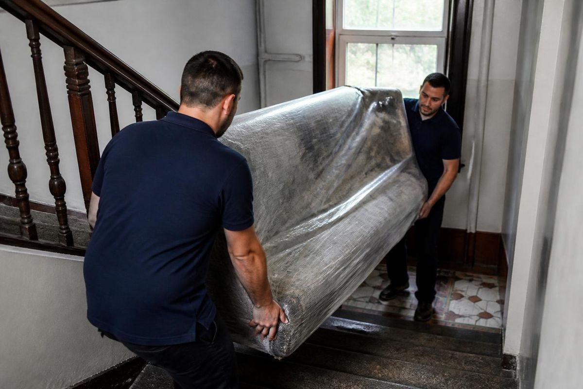 Mudanzas de pisos en Bizkaia: dos mozos bajando un sofá protegido por la escalera de un edificio