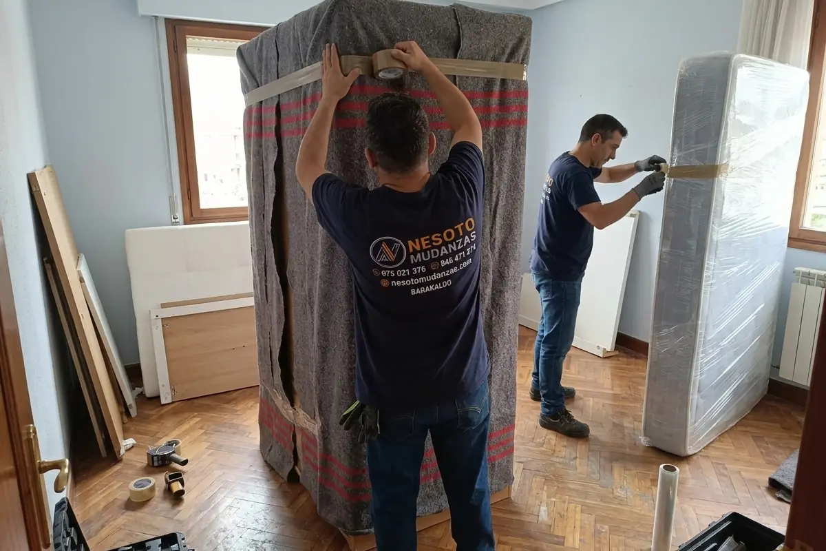 Operarios de NESOTO protegiendo un armario con mantas y un colchón con plástico antes de guardarlos