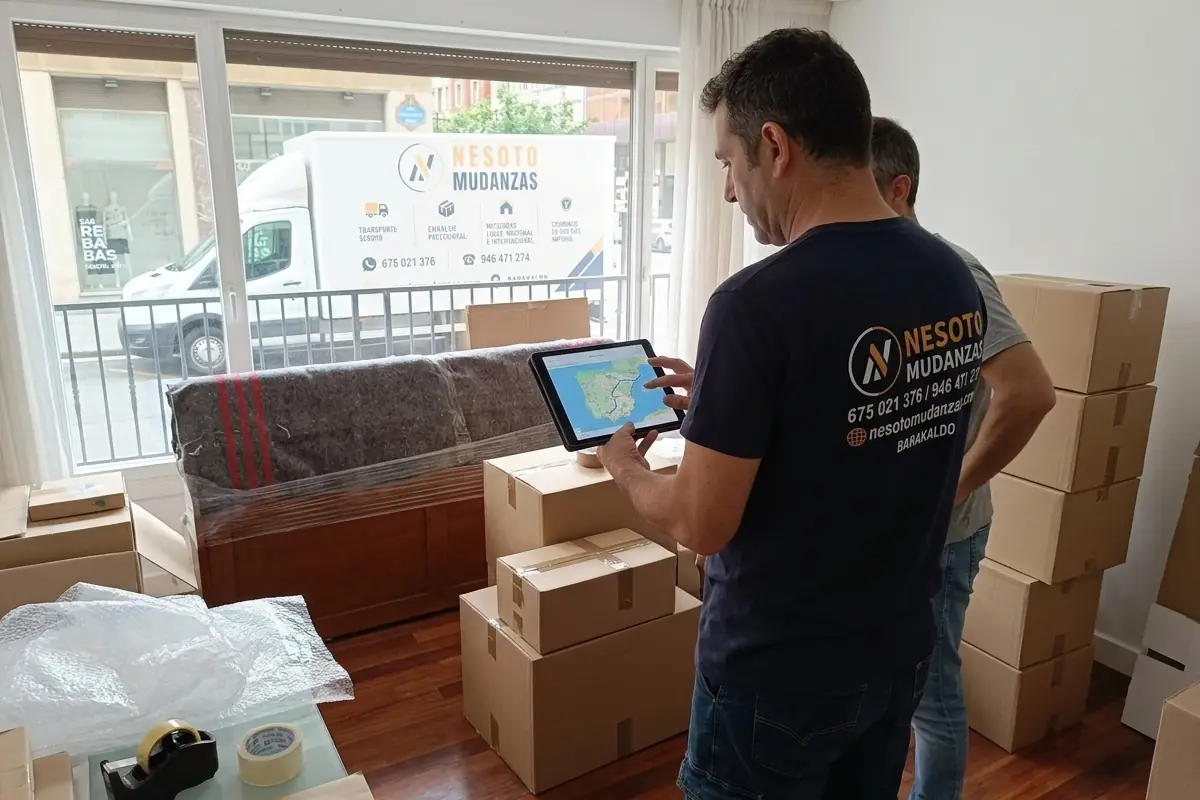 Operario de NESOTO con una tablet con la ruta de una mudanza nacional, junto a cajas y muebles protegidos